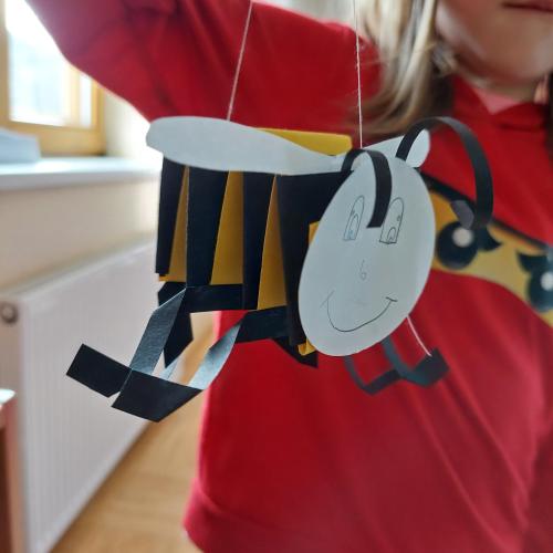Biene hängt an einem Faden, Kind hält diese "fliegende" Biene in der Hand