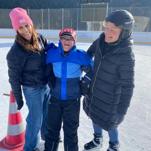 2 Assistentinnen halten einen Bub mit erhöhtem Förderbedarf, alle tragen Eislaufschuhe