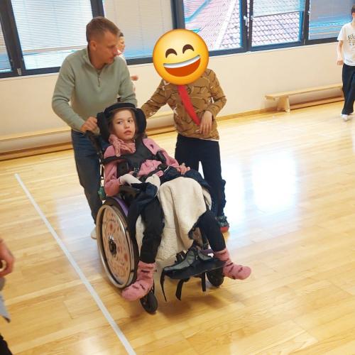 im Bewegungsraum: Lehrer schiebt Mädchen im Rollstuhl