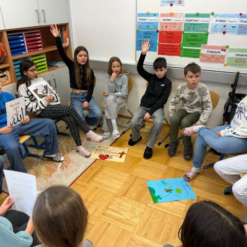 im Sitzkreis, manche Kinder zeigen auf um eine Frage zu stellen
