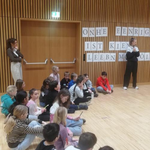 Kinder sitzen in großem Raum und hören zu