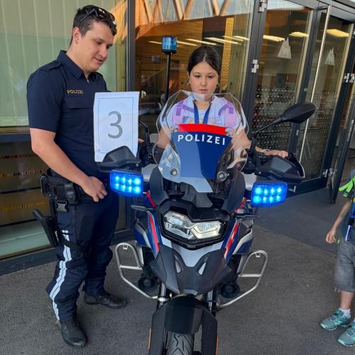 aufgeregt sitzt ein Mädchen auf dem Motorrad, Polizist erklärt ihr alles