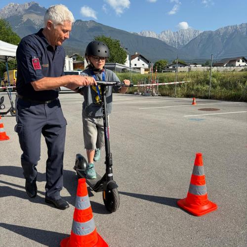 Bub fährt mit dem E-Scooter, ein Polizist unterstützt ihn dabei