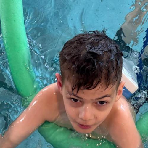 Bub schwimmt mit einer Schwimmnudel 