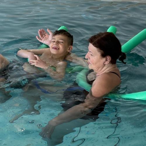 Bub übt das Rückenschwimmen mit der Schwimmnudel und der Lehrerin