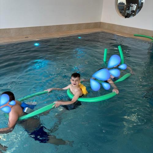 Kinder schwimmen hintereinander und halten sich an der Schwimmnudel des Vorderen fest