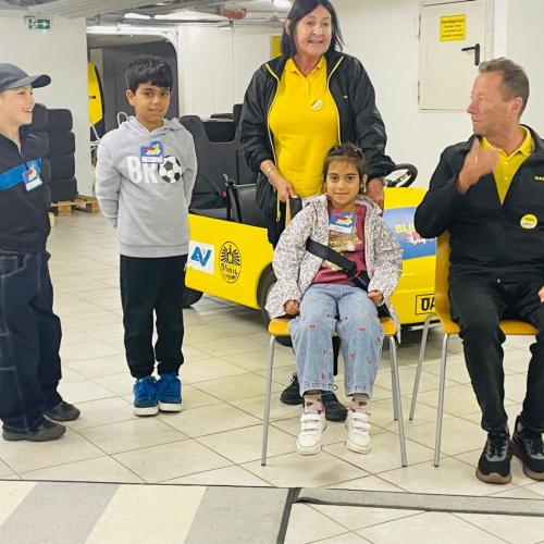 Die Mitarbeiter zeigen an einem Kind, wie man sich im Auto richtig anschnallt