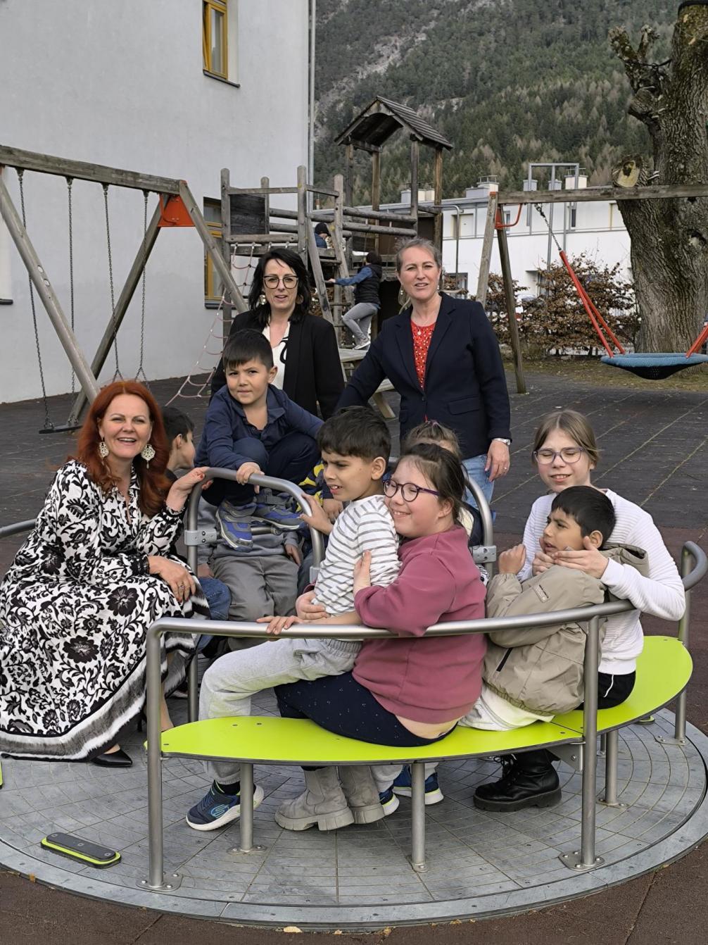 Landesrätin mit SQM, Schulleiterin und mehreren Kindern im inklusiven Karussel