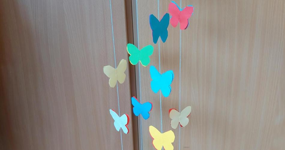 Schmetterlinge aus buntem Tonpapier sind auf einem dünnen Garn aufgefädelt und hängen an einem weißen Kartonkreis