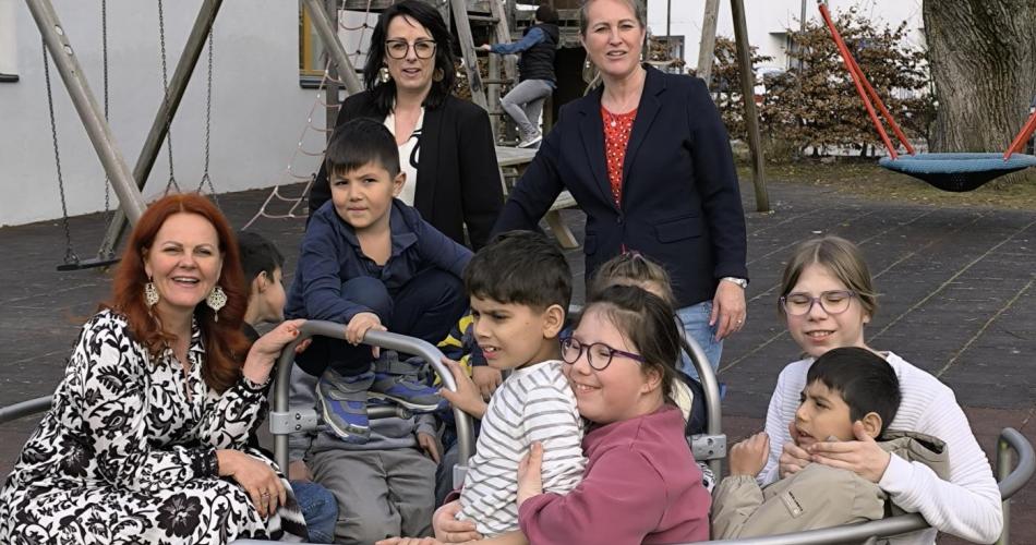 Landesrätin mit SQM, Schulleiterin und mehreren Kindern im inklusiven Karussel